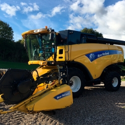 Køb og salg af New Holland mejetærsker parkeret på grusvej med grønne marker i baggrunden